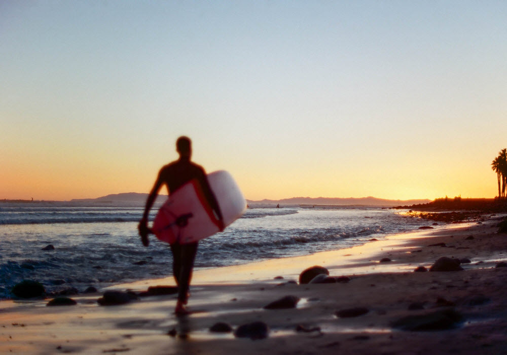 Surfer walking on the beach in Ventura, California at sunset. 