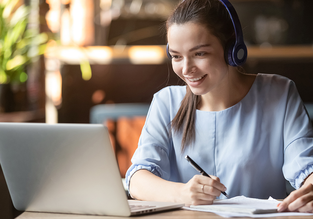 Happy woman looking at laptop and writing notes.