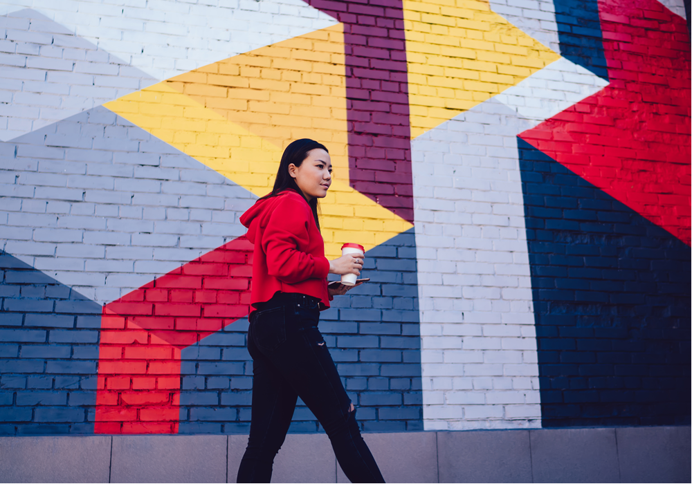 Woman walking next to wall mural with coffee in hand.