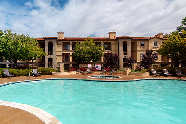 Outdoor swimming pool area with lounge seating, umbrellas, and lush landscaping.
